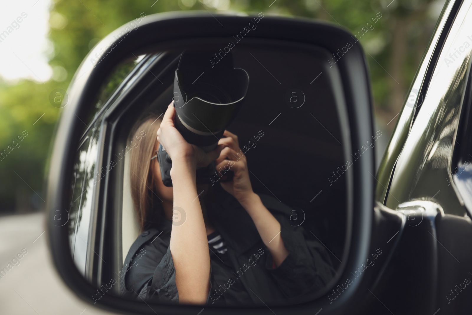 Photo of Private detective with camera spying from auto, view through car side mirror