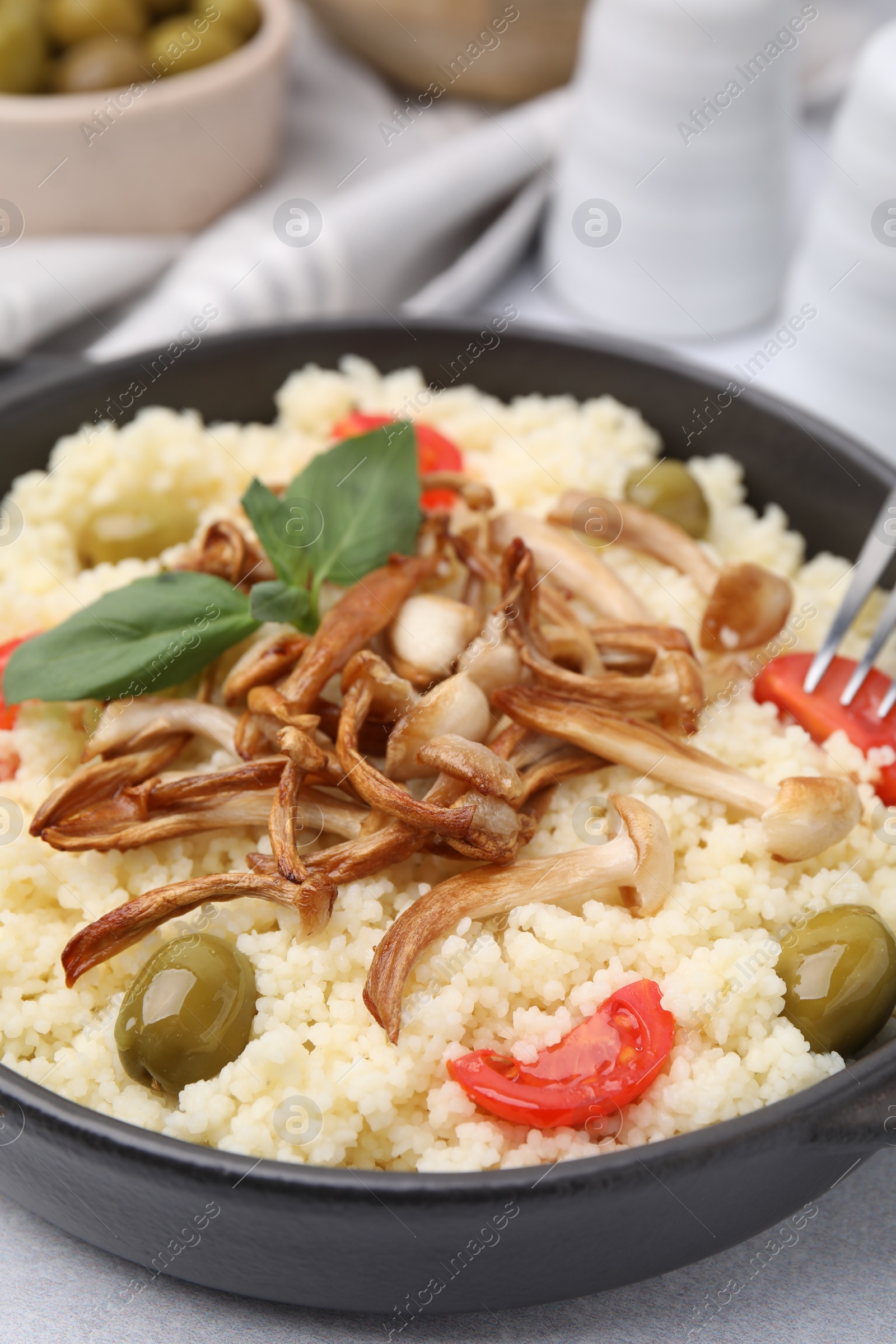 Photo of Tasty couscous with mushrooms, olives and tomatoes served on grey table, closeup