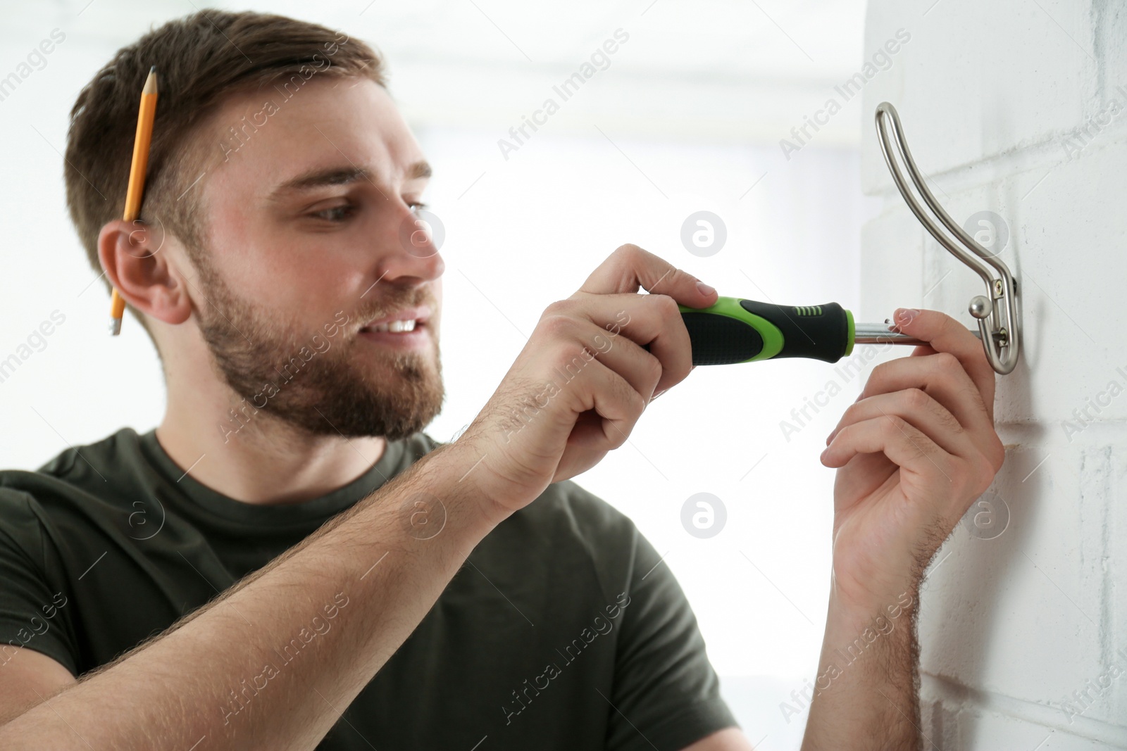 Photo of Young working man fixing clothes hook on wall at home
