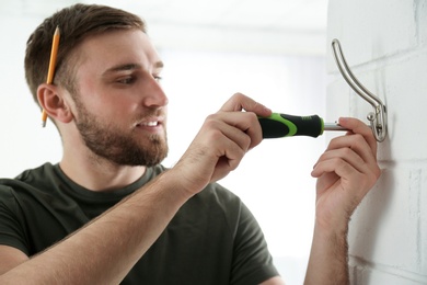 Photo of Young working man fixing clothes hook on wall at home