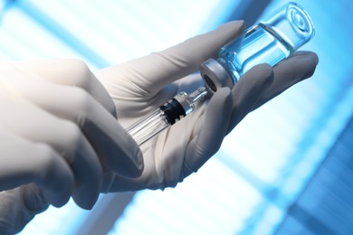 Photo of Woman filling syringe with vaccine from vial on blurred background, closeup