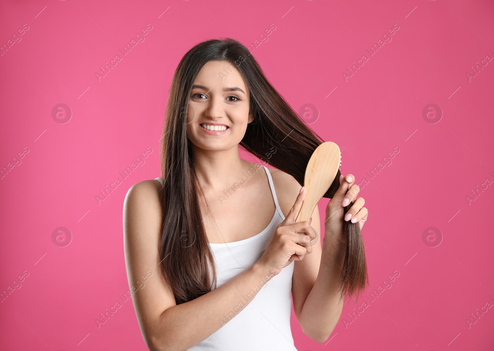 Photo of Beautiful smiling young woman with hair brush on color background