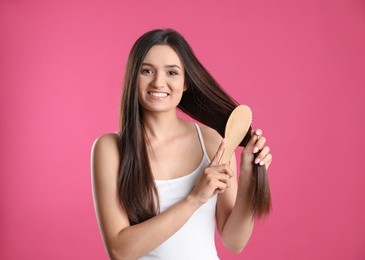 Beautiful smiling young woman with hair brush on color background