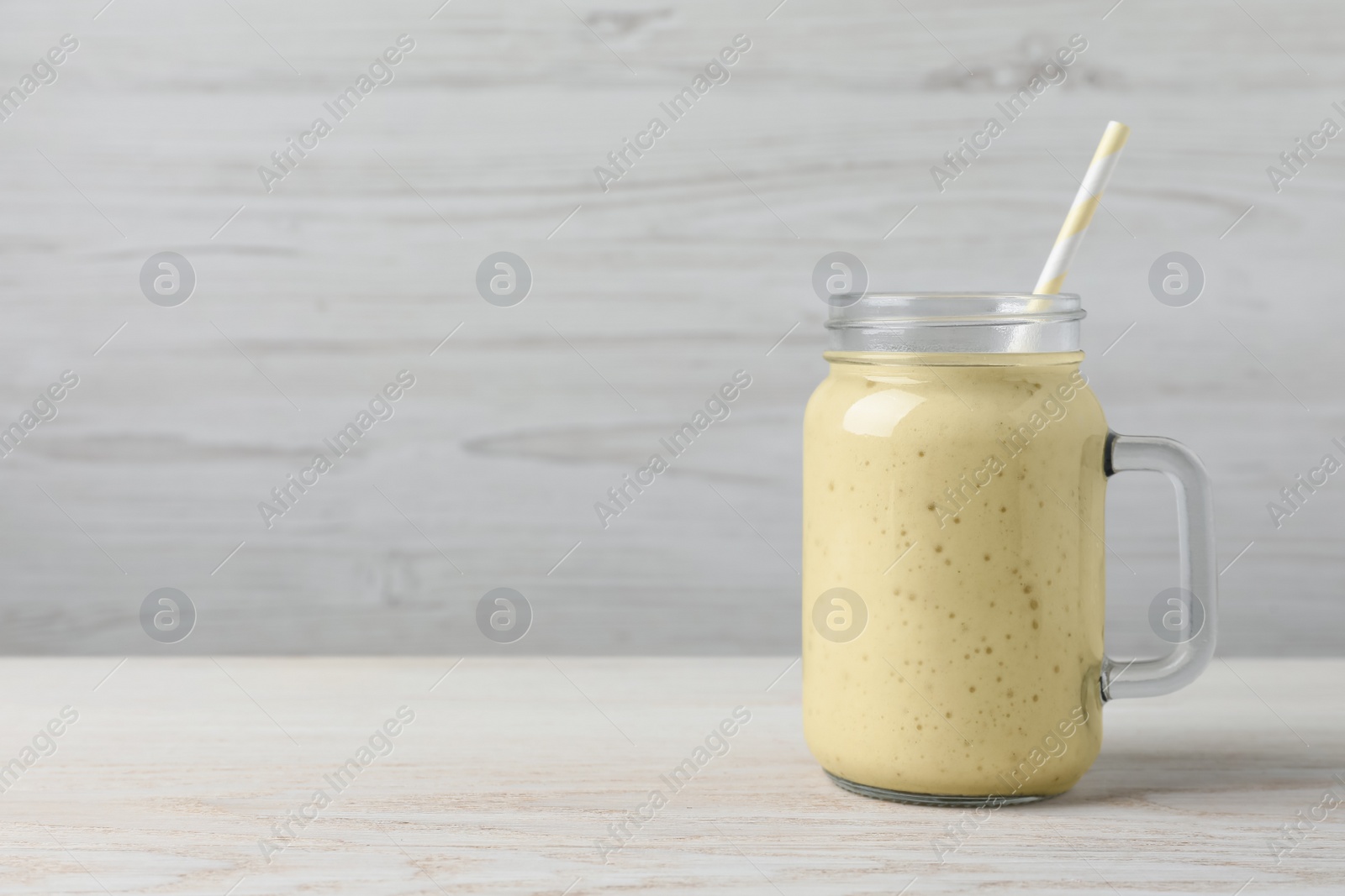 Photo of Mason jar with delicious fruit smoothie on white wooden table. Space for text
