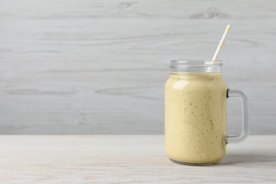 Photo of Mason jar with delicious fruit smoothie on white wooden table. Space for text