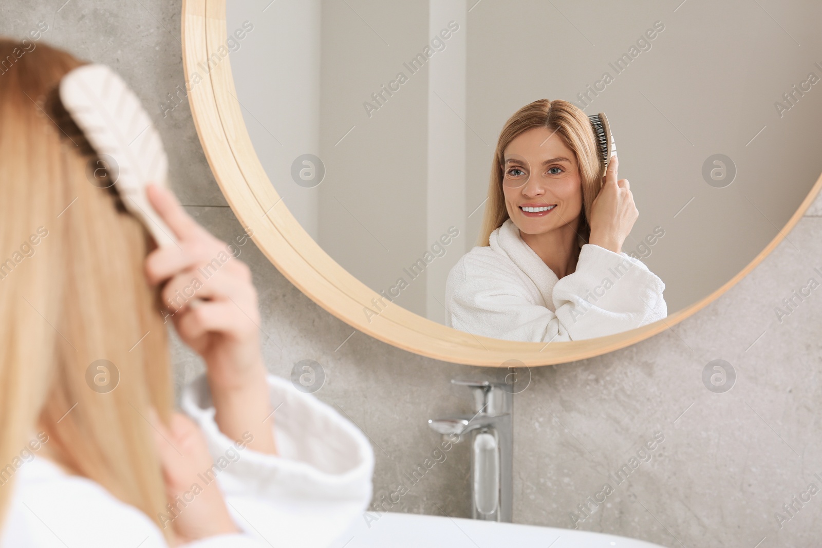 Photo of Beautiful woman brushing her hair near mirror in bathroom