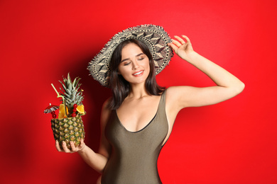 Beautiful woman in stylish swimsuit holding tropical cocktail on red background