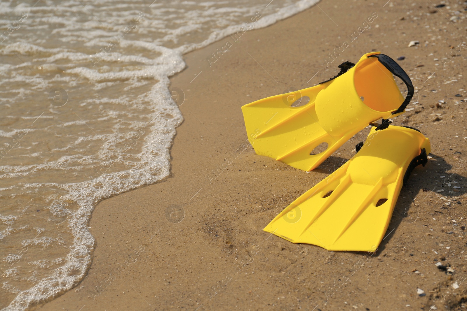 Photo of Pair of yellow flippers on sand near sea. Space for text