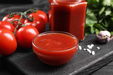 Delicious ketchup and tomatoes on black wooden table, closeup. Tomato sauce