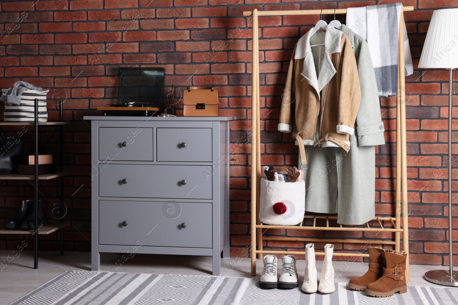 Photo of Beautiful hallway interior with coat rack, chest of drawers and shoe storage bench near red brick wall