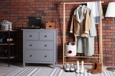 Photo of Beautiful hallway interior with coat rack, chest of drawers and shoe storage bench near red brick wall