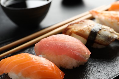 Serving board with delicious nigiri sushi and soy sauce on black table, closeup