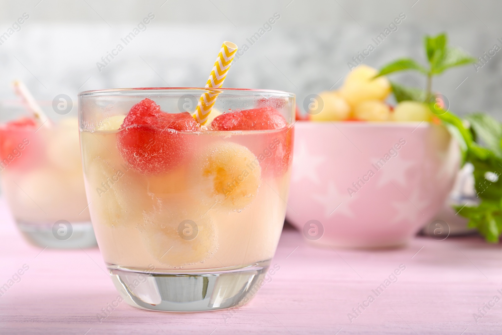 Photo of Glass of melon and watermelon ball cocktail on pink wooden table, closeup. Space for text