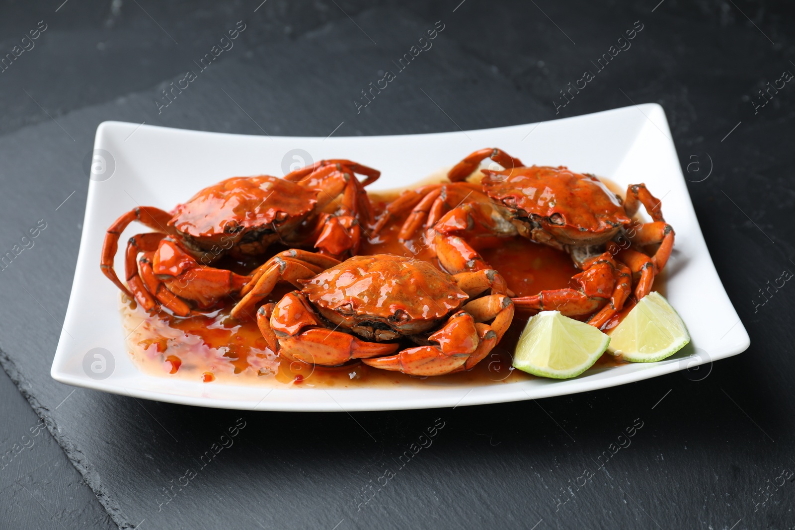 Photo of Delicious boiled crabs with sauce and lime on black textured table