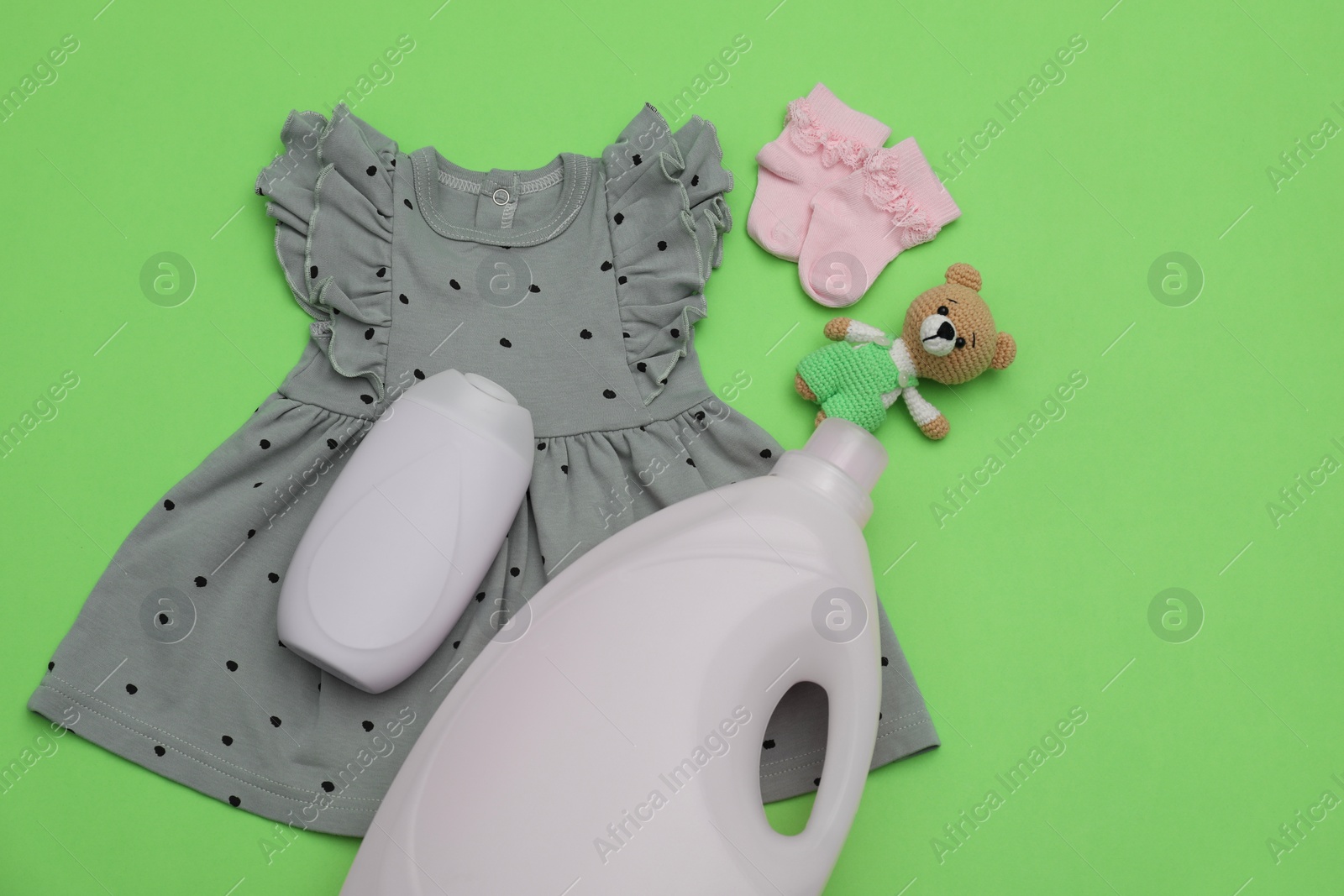 Photo of Bottles of laundry detergents, baby clothes and toy bear on light green background, flat lay. Space for text