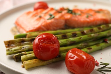 Tasty grilled asparagus, tomatoes and salmon on plate, closeup