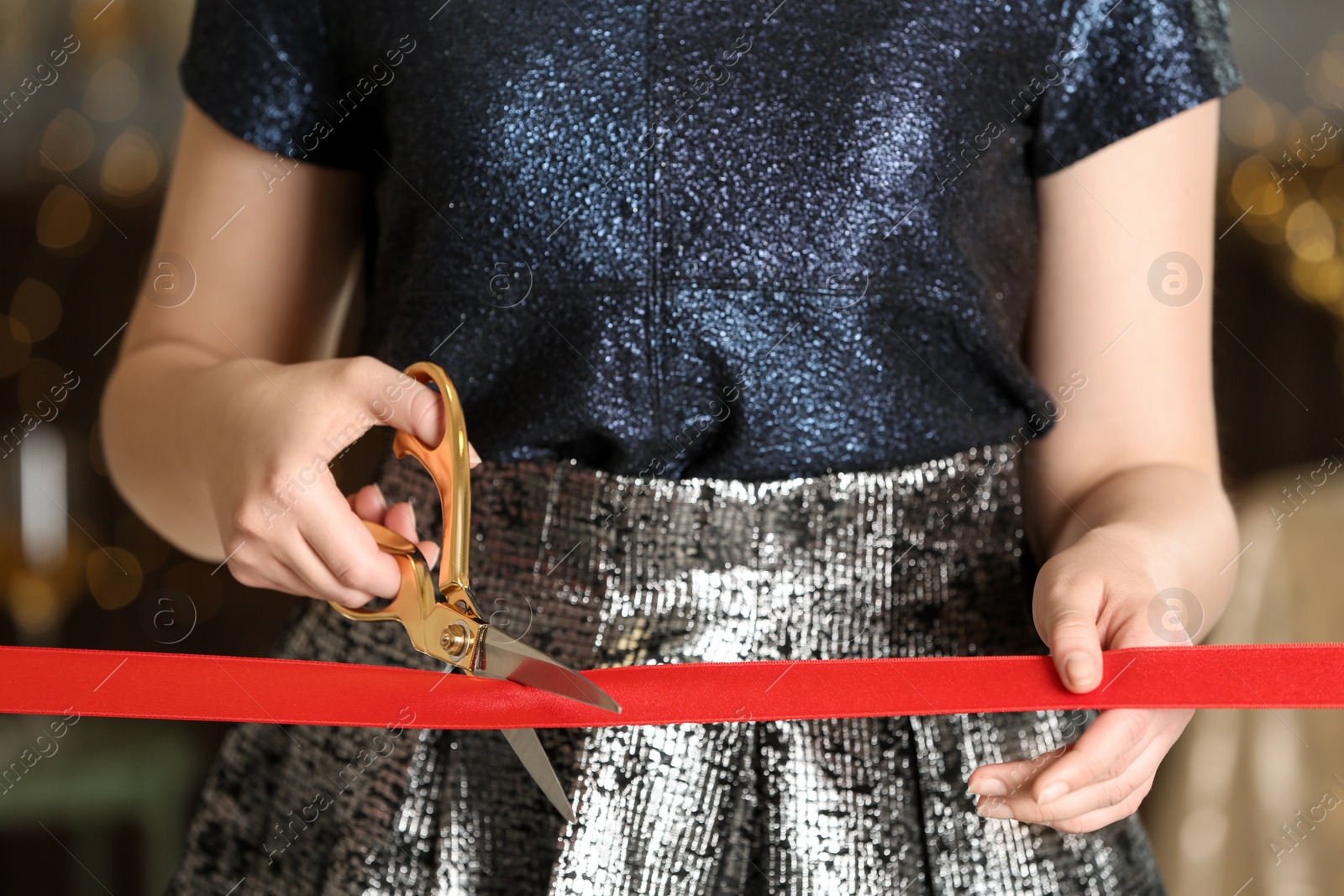 Photo of Woman cutting red ribbon with scissors indoors at ceremonial event