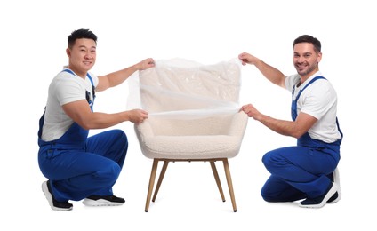 Workers covering armchair with plastic film on white background