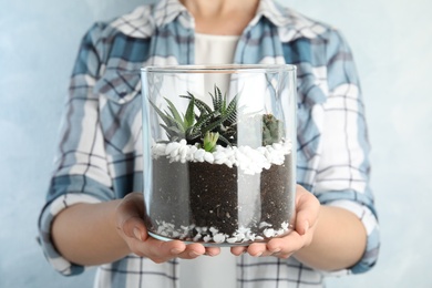 Young woman holding florarium with different succulents on color background, closeup