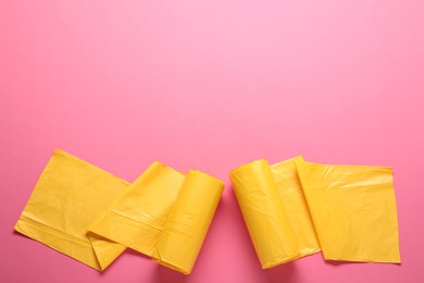 Photo of Rolls of yellow garbage bags on pink background, flat lay. Space for text
