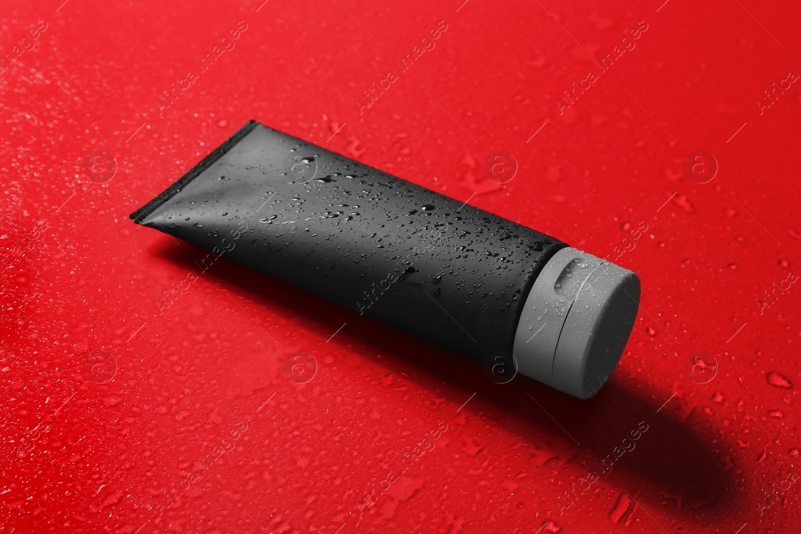 Photo of Black tube on wet color surface, space for design. Men's cosmetic product