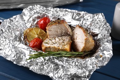 Photo of Pieces of delicious meat baked in foil with tomatoes on blue wooden table, closeup