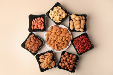 Photo of Bowls with dried fruits and nuts on beige background, flat lay