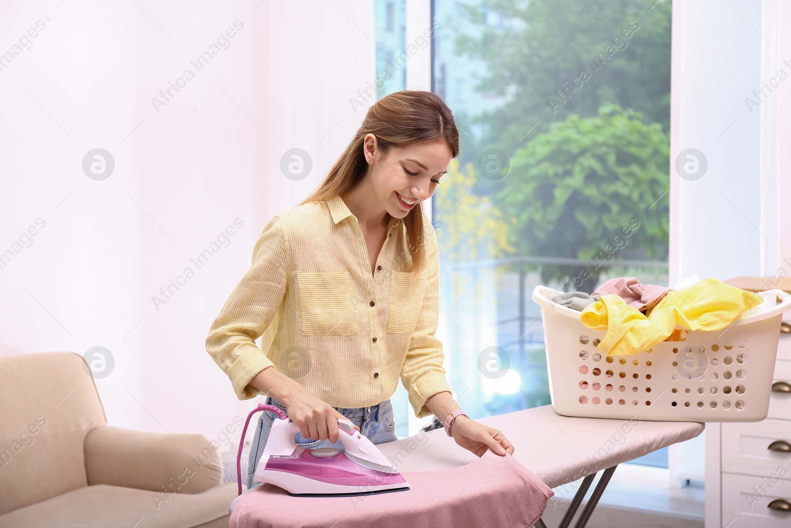 Photo of Young pretty woman ironing clean laundry indoors