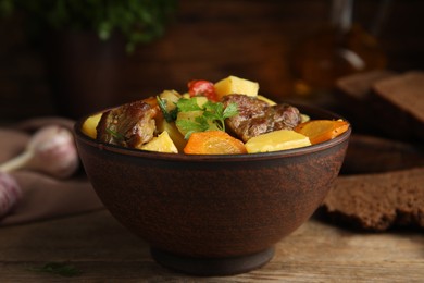 Photo of Tasty cooked dish with potatoes in earthenware served on wooden table