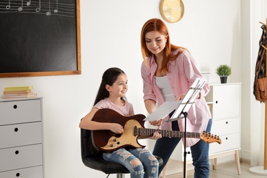 Photo of Little girl playing guitar with her teacher at music lesson. Learning notes