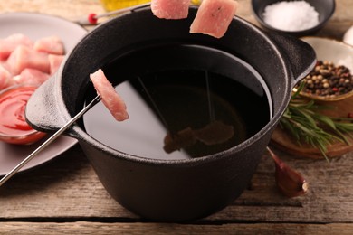 Fondue pot with oil, forks, raw meat pieces and other products on wooden table, closeup