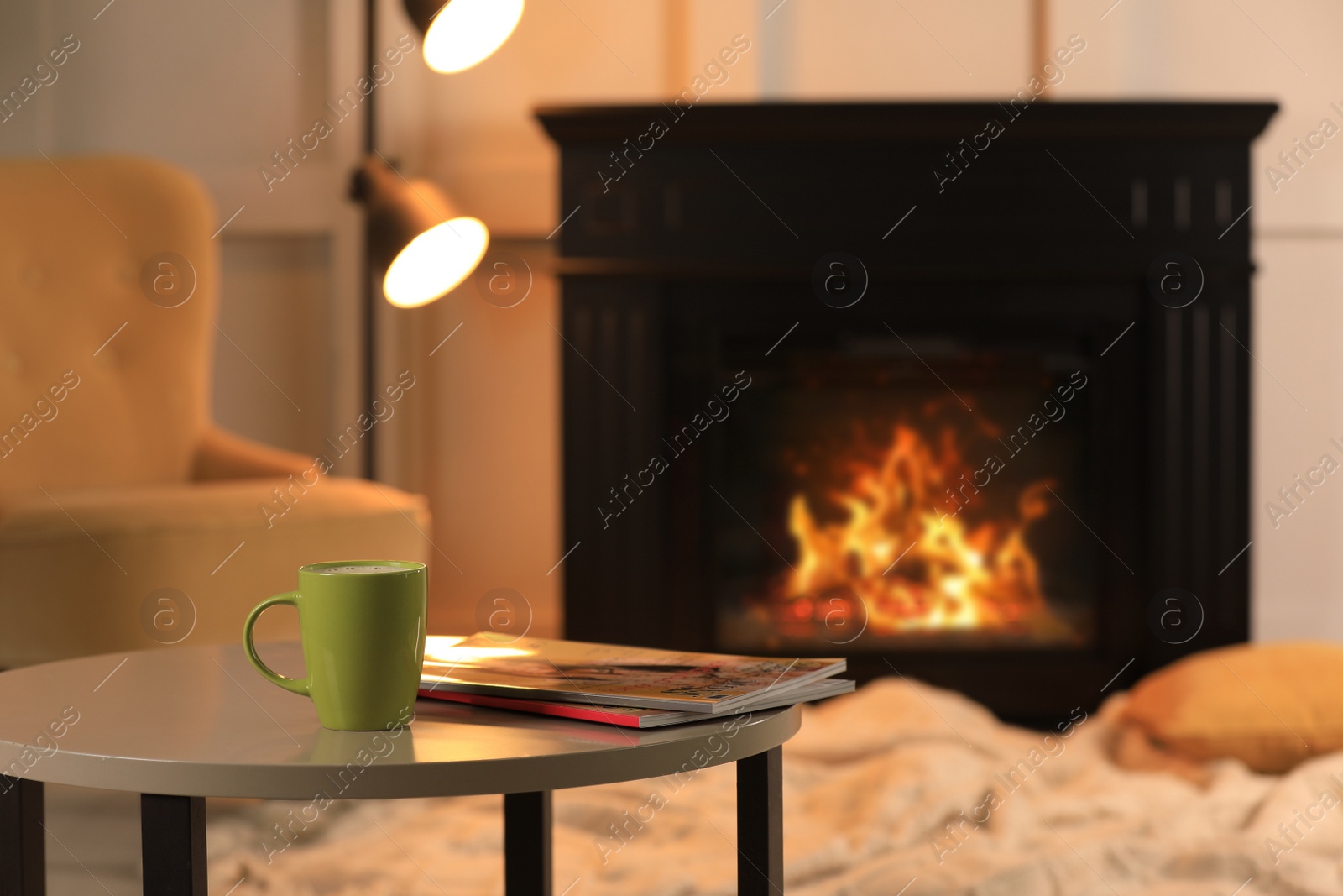 Photo of Cup of hot drink and magazines on table near fireplace at home, space for text. Cozy atmosphere