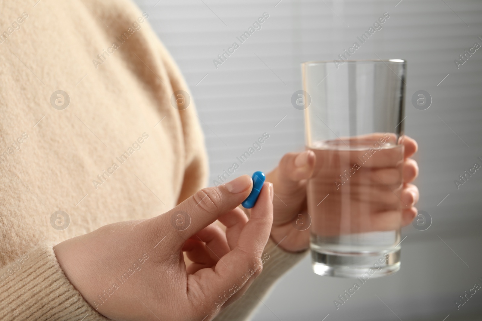 Photo of Woman with glass of water and pill on light background, closeup