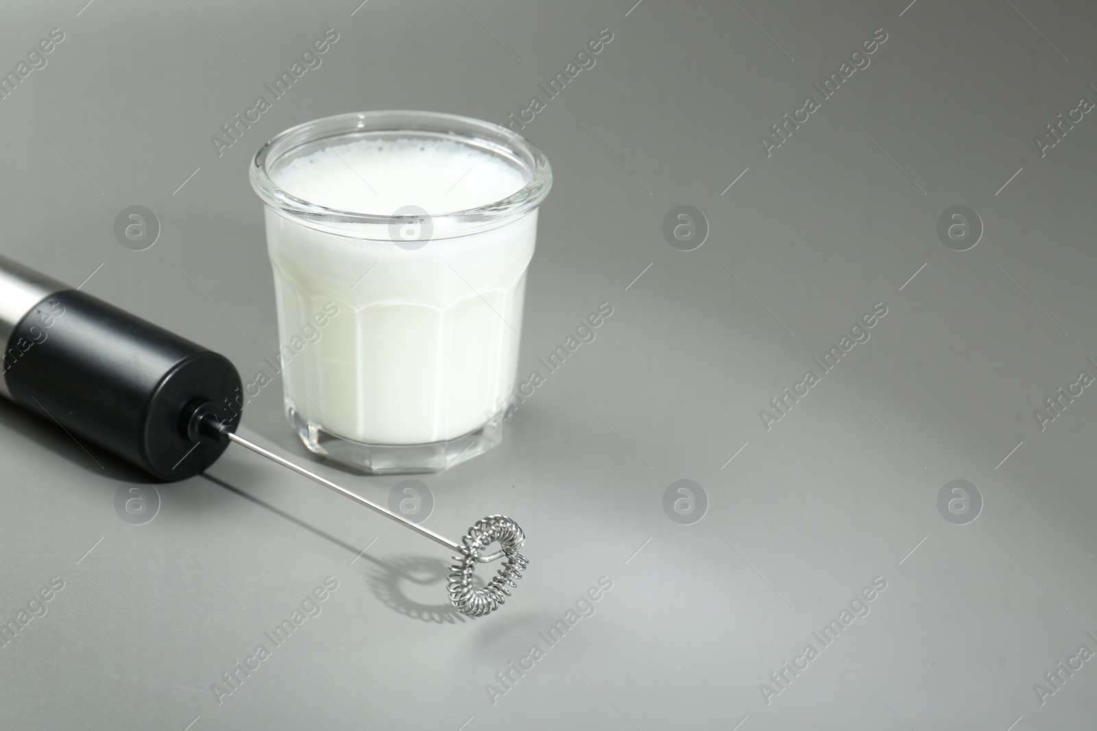 Photo of Mini mixer (milk frother) and whipped milk in glass on grey background. Space for text