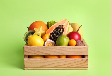 Different tropical fruits in wooden box on green background