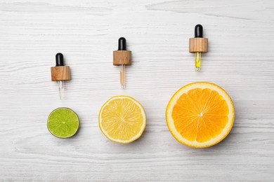 Photo of Pipettes with citrus essential oils and fresh fruits on white wooden table, flat lay