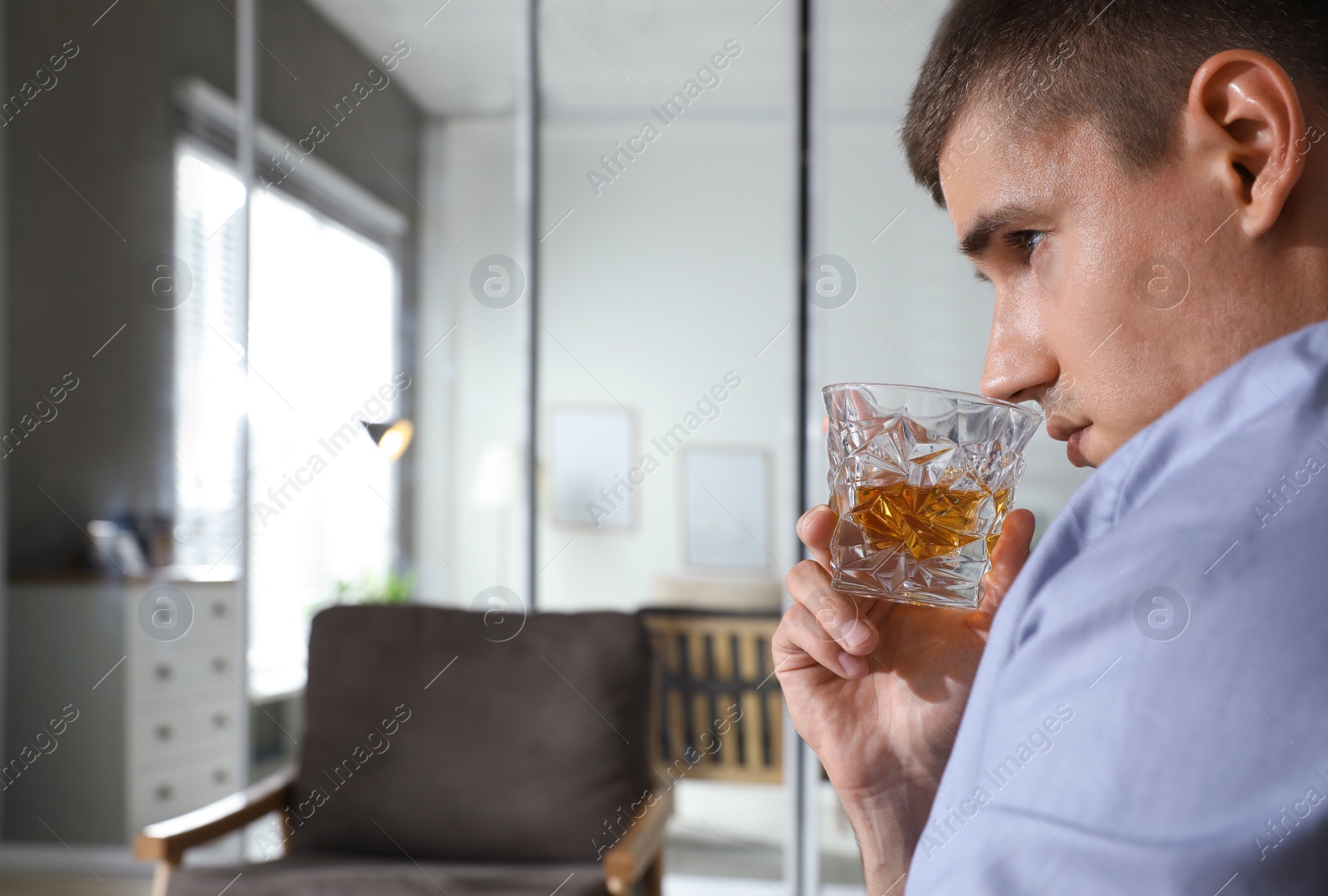 Photo of Young man with glass of whiskey at home. Space for text