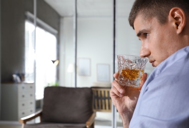 Young man with glass of whiskey at home. Space for text