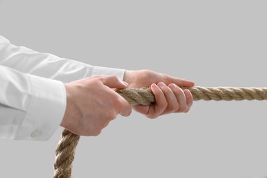 Dispute concept. Man pulling rope on light grey background, closeup