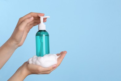 Woman with bottle of care product and cleansing foam on light blue background, closeup. Space for text