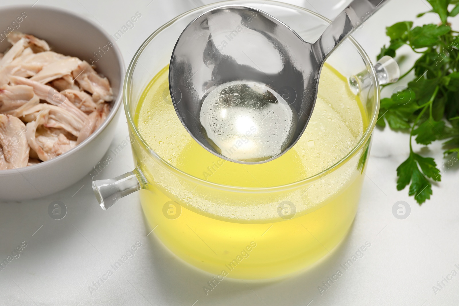 Photo of Glass pot with tasty bouillon, chicken and parsley on white marble table