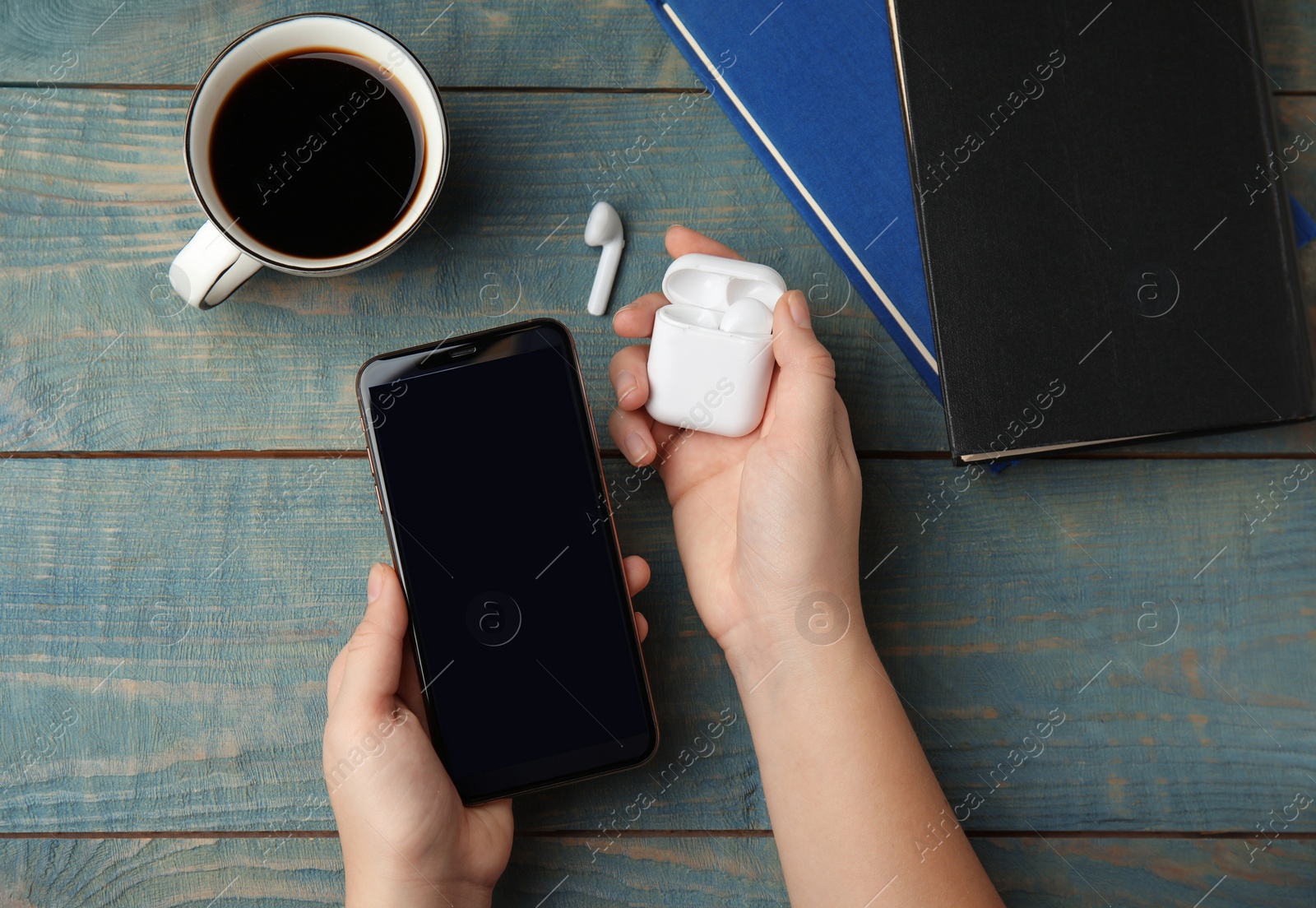 Photo of Woman holding mobile phone over light blue wooden table with books, top view