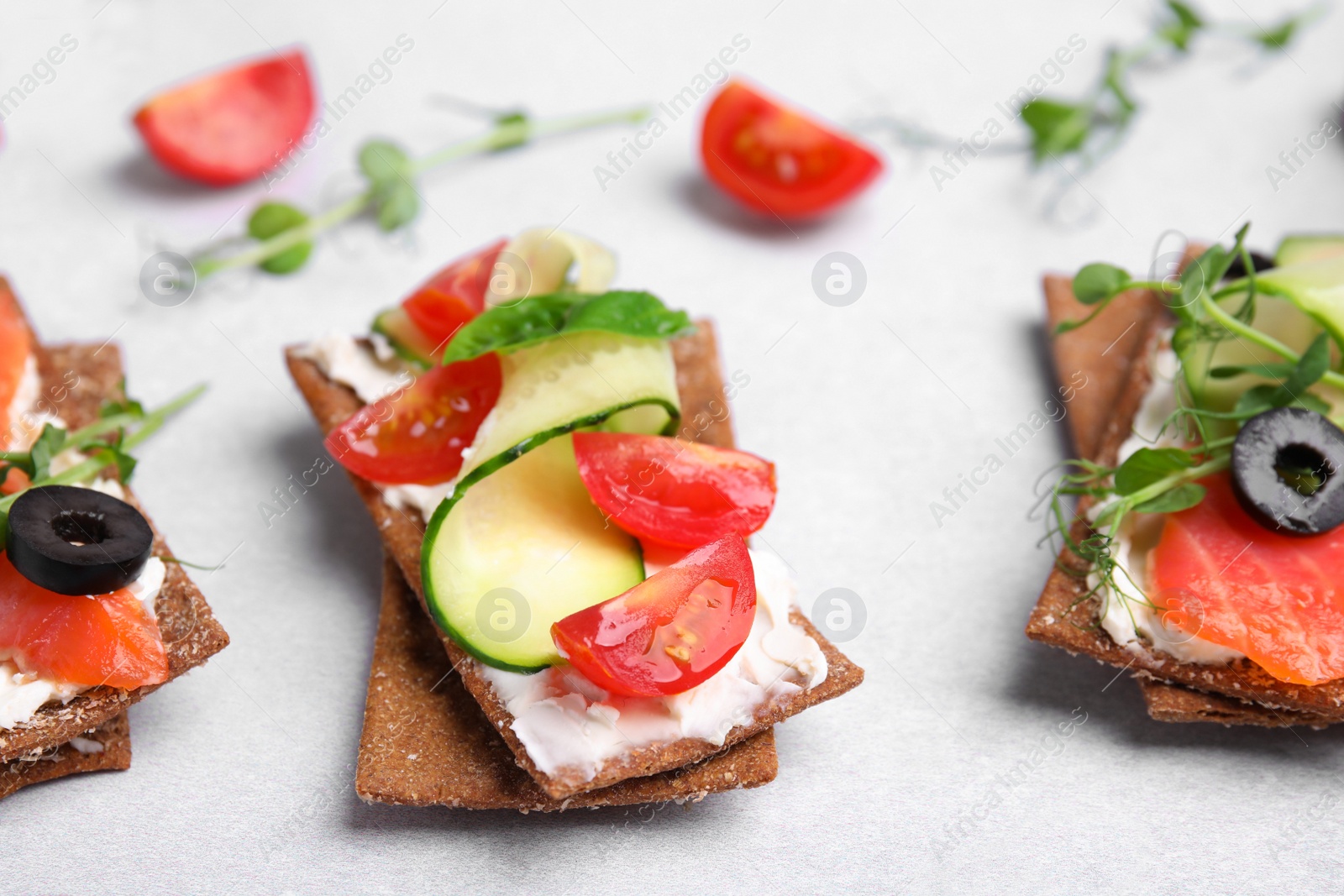Photo of Tasty rye crispbreads with salmon, cream cheese and vegetables on light grey table, closeup