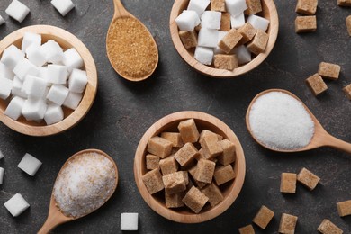 Photo of Bowls and spoons with different types of sugar on gray table, flat lay