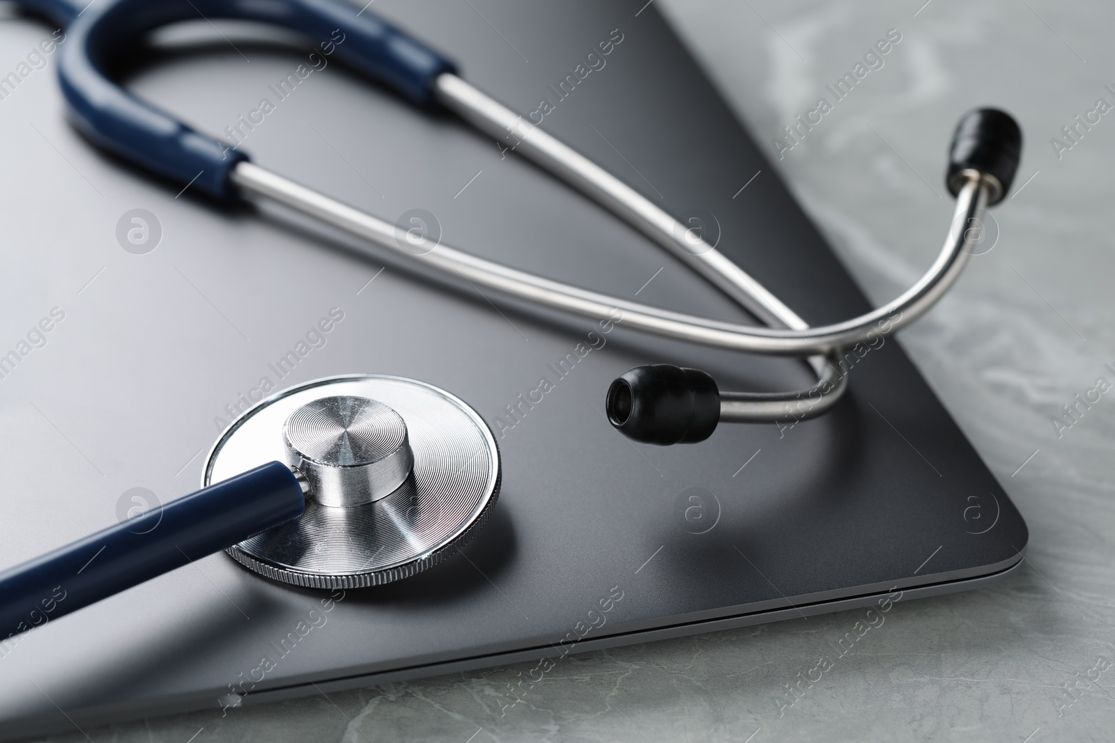 Photo of Modern laptop and stethoscope on grey table, closeup
