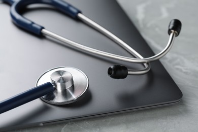 Modern laptop and stethoscope on grey table, closeup