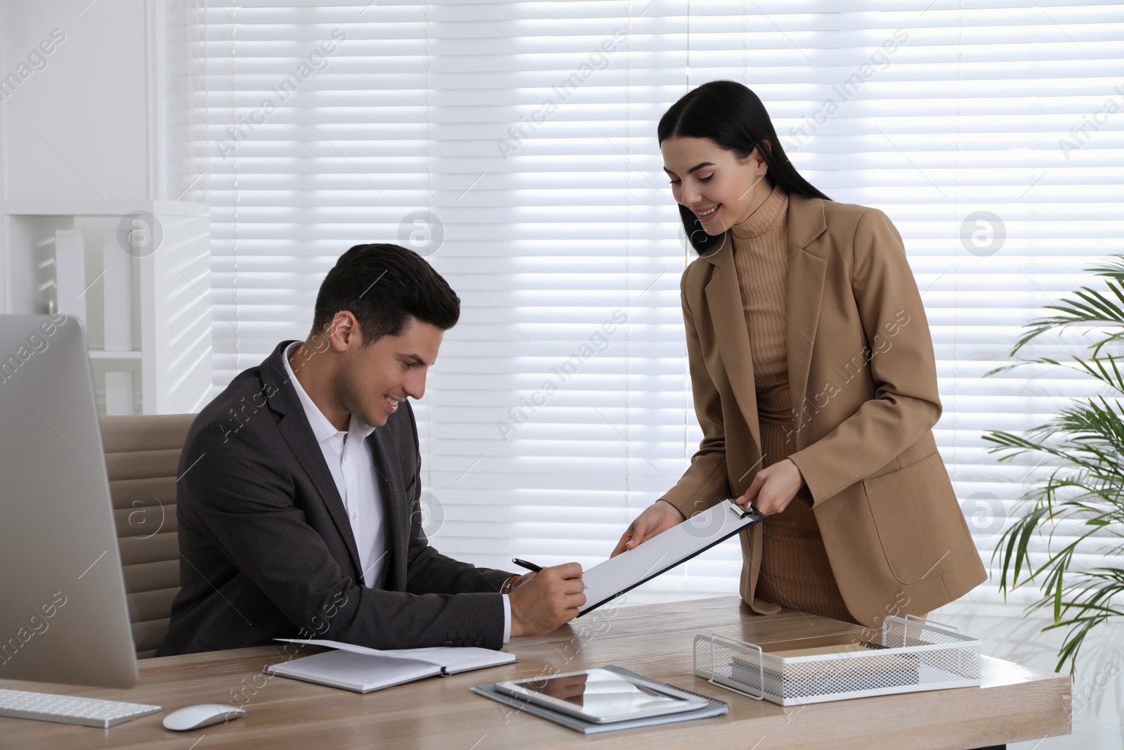 Photo of Secretary bringing document for signature to her boss  in office