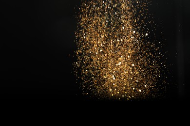 Photo of Shiny golden glitter falling down on black background. Bokeh effect