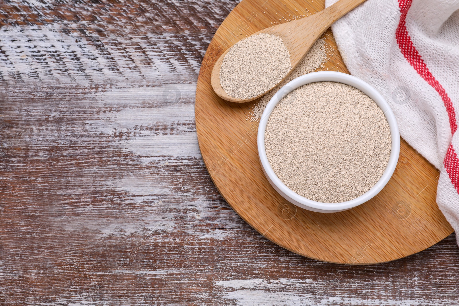 Photo of Bowl and spoon with active dry yeast on wooden table, top view. Space for text