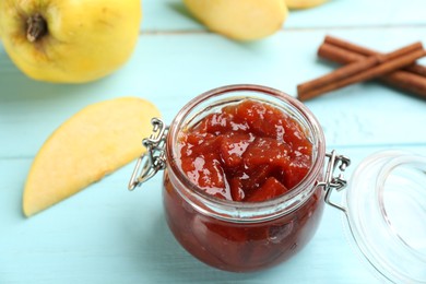 Photo of Delicious quince jam, fruits and cinnamon on light blue wooden table